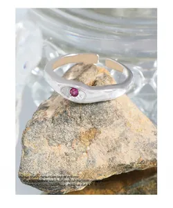 Macro shot of silver minimalist ring with red gemstone set on a natural stone