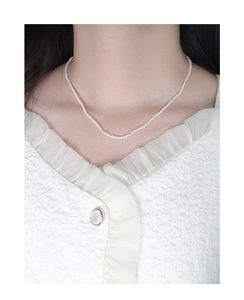 Close-up of minimalist small white pearl necklace worn with elegant textured blouse