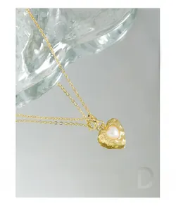 Close-up of heart pendant with hammered texture and pearl inlay on a golden chain