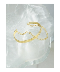 Macro detail of gold textured cuff bracelet with chain accent on a frosted base