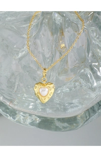 Macro detail of gold-plated textured heart pendant with central pearl inlay on glass