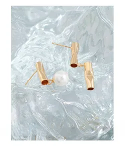 Detailed view of asymmetric gold bamboo style stud earrings with elegant white pearls