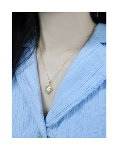Detail of a textured gold heart pendant featuring a centered round white pearl inlay