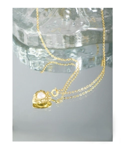 Macro shot of gold heart pendant with hammered texture and pearl on a reflective surface