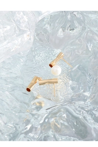Detailed macro view of asymmetric gold tube earrings with a white iridescent pearl