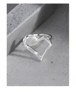 Detailed close-up of irregular silver heart ring with melted texture on grey cement block