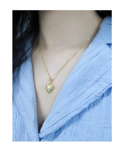 Close-up of a gold heart pendant necklace with pearl inlay on a model's neck