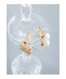 Detail of minimalist gold-plated tube earrings with white pearls on a glass display