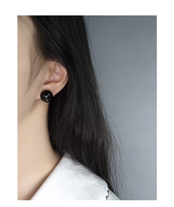 Close-up of a high-gloss black agate sphere stud earring worn on an ear for detail