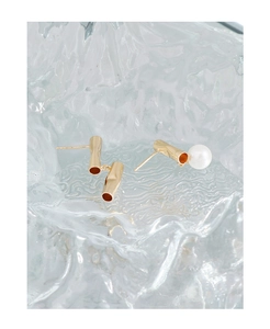 Close-up of asymmetric gold-plated earrings with metal cylinder and pearl detail