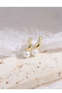 Macro shot of irregular gold earrings with white pearls on a textured stone base