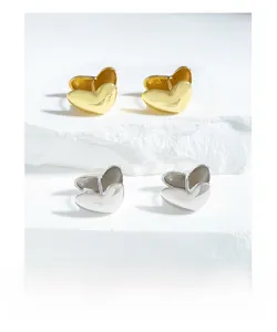 Macro detail of high-polish gold and silver heart earrings on a natural stone surface
