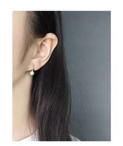 Detail of elegant gold drop earring with a single round white pearl worn by a model