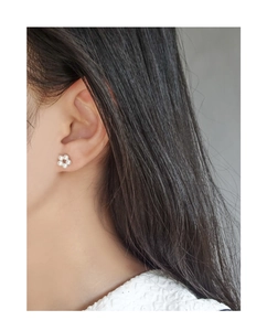 Detailed close-up of a delicate floral pearl stud earring worn on a model's ear lobe
