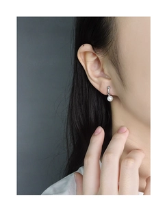 Detail shot of a geometric S925 silver stud earring with a white pearl on a model's ear