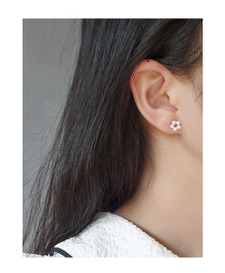 Macro shot of minimalist pearl flower stud earrings worn on model earlobe