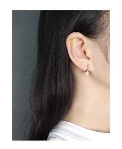 Close-up of a minimalist gold hook earring with a round white pearl on a female model