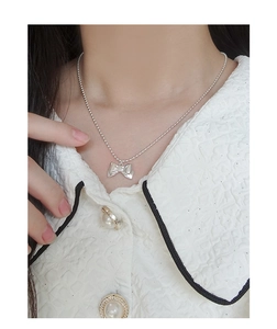 Macro detail of silver bow pendant necklace with polished bead chain on model neck
