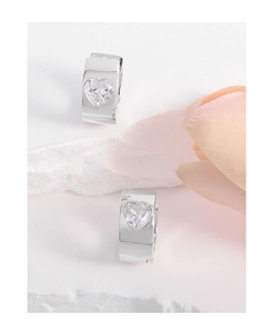 Detail of heart-shaped zircon inlay on polished silver hoop earrings over stone decor