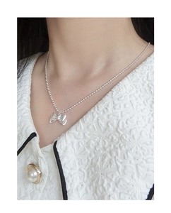 Detail of silver S925 beaded chain necklace with bow pendant worn by a model