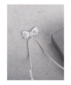 Detailed view of silver bow pendant with round bead chain on a grey stone texture