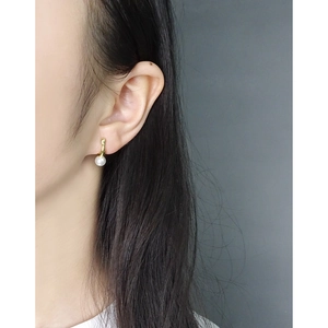Elegant geometric gold pearl stud earrings worn by a model against a dark background