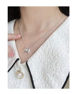 Detail view of a polished silver bow pendant on a delicate beaded chain worn by a model