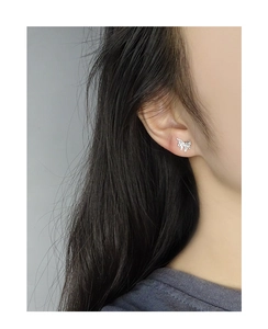 Detail view of silver butterfly stud earrings with textured finish on model ear