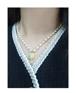 Détail d'un collier de perles avec pendentif soleil doré et opale verte sur modèle