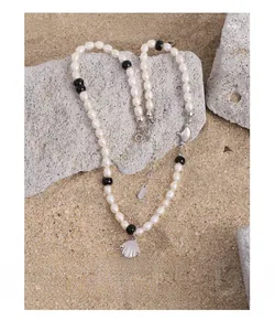 Détail du poinçon S925 sur collier en perles avec pendentif coquillage sur sable