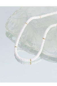 Gros plan d'un collier en perles de céramique blanche et espaceurs dorés sur verre ondulé