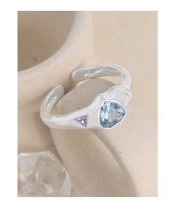 Détail macro d'une bague en argent S925 avec gemme bleue en cœur et anneau ondulé