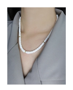 Détail d'un collier en perles de céramique blanche avec intercalaires dorés porté par une femme