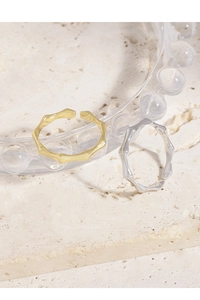 Detailed view of gold and silver S925 bamboo rings on a beige stone surface