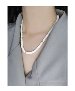 Gros plan d'un collier en perles de céramique blanche avec anneaux dorés sur un mannequin