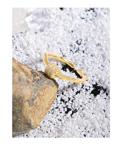 Close-up of a gold ring featuring a pavé-set zircon cylinder charm on a polished band