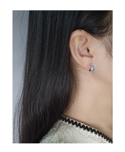 Dettaglio di un orecchino in argento con zircone blu indossato sul lobo dell'orecchio