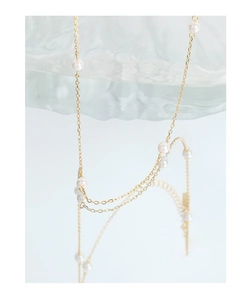 Close-up of minimalist gold chain pearl necklace reflecting on wave-textured glass