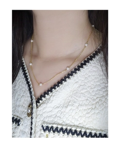 Close-up of a delicate gold station necklace with white pearls worn on a female neck