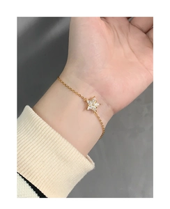 Close-up of a gold snowflake zircon bracelet worn on wrist with elegant minimalist background