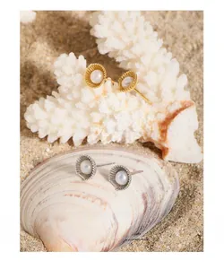 Detail view of gold and silver shell pearl earrings on white coral and sand background