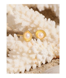 Macro shot of gold shell pearl earrings featuring detailed scallop texture on beach sand