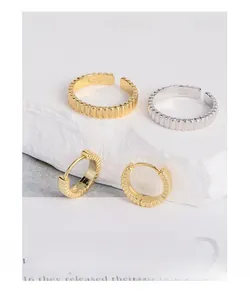 Detailed view of S925 sterling silver wavy rings and gold earrings on a stone base