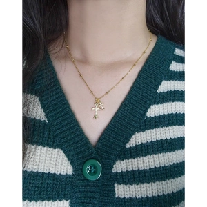 Elegant gold double cross pendant necklace with zircon stones on a knit cardigan background