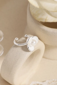 Macro detail of silver flower ear cuff with white enamel petals and a center pearl