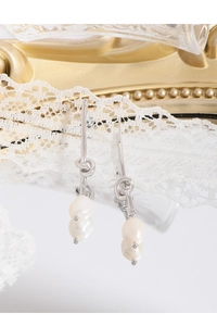 Macro shot of silver knot earrings with white baroque pearls on delicate white lace