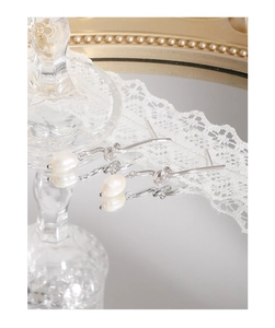 Detailed view of silver knot drop earrings with round white pearl reflecting on mirror