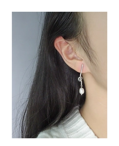 Silver knot earring with a white drop pearl shown worn by a model in a minimalist style