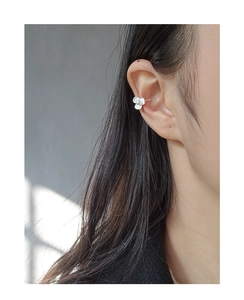 Detail of a white floral ear cuff with a central pearl on a model's ear