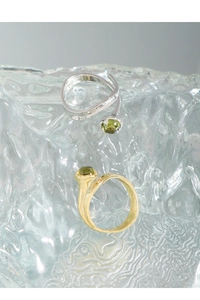 Detail view of S925 silver and gold rings with green crystal stones on glass texture